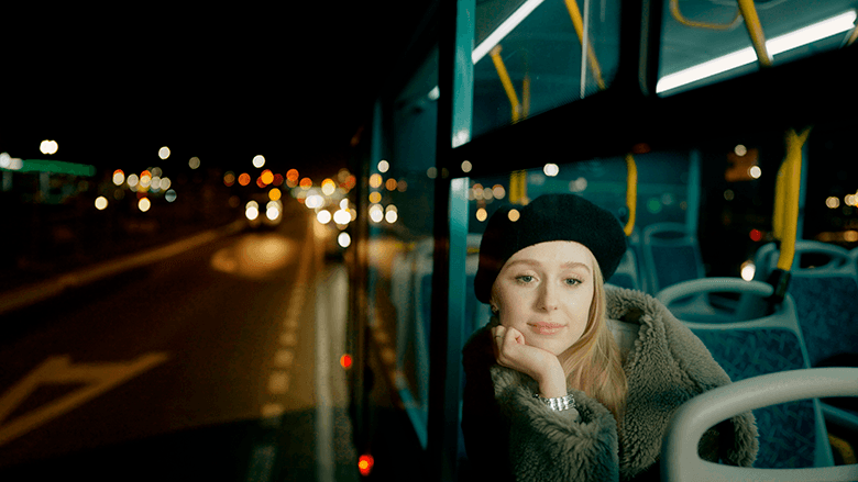 Девушка смотрит в окно автобуса, кадр снаружи, ночь